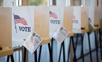 Voting booths with an American flag poster that reads VOTE