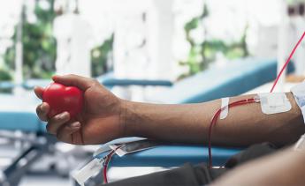 A male blood donor squeezing a heart-shaped red ball with an attached catheter.