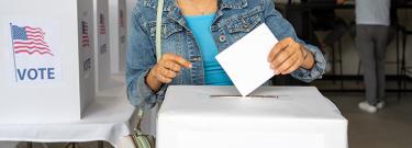 Young black woman dropping her ballot into a ballot box at a voting center