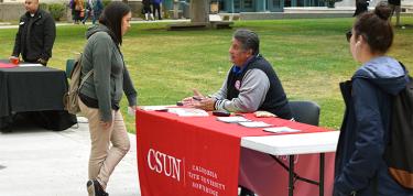 CSUN representative talking to a student in the quad as other students walk by