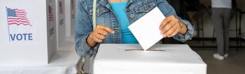 Young black woman dropping her ballot into a ballot box at a voting center