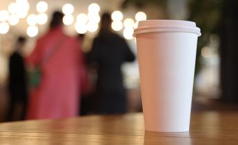 A coffee cup in the foreground with a group of people talking in the background